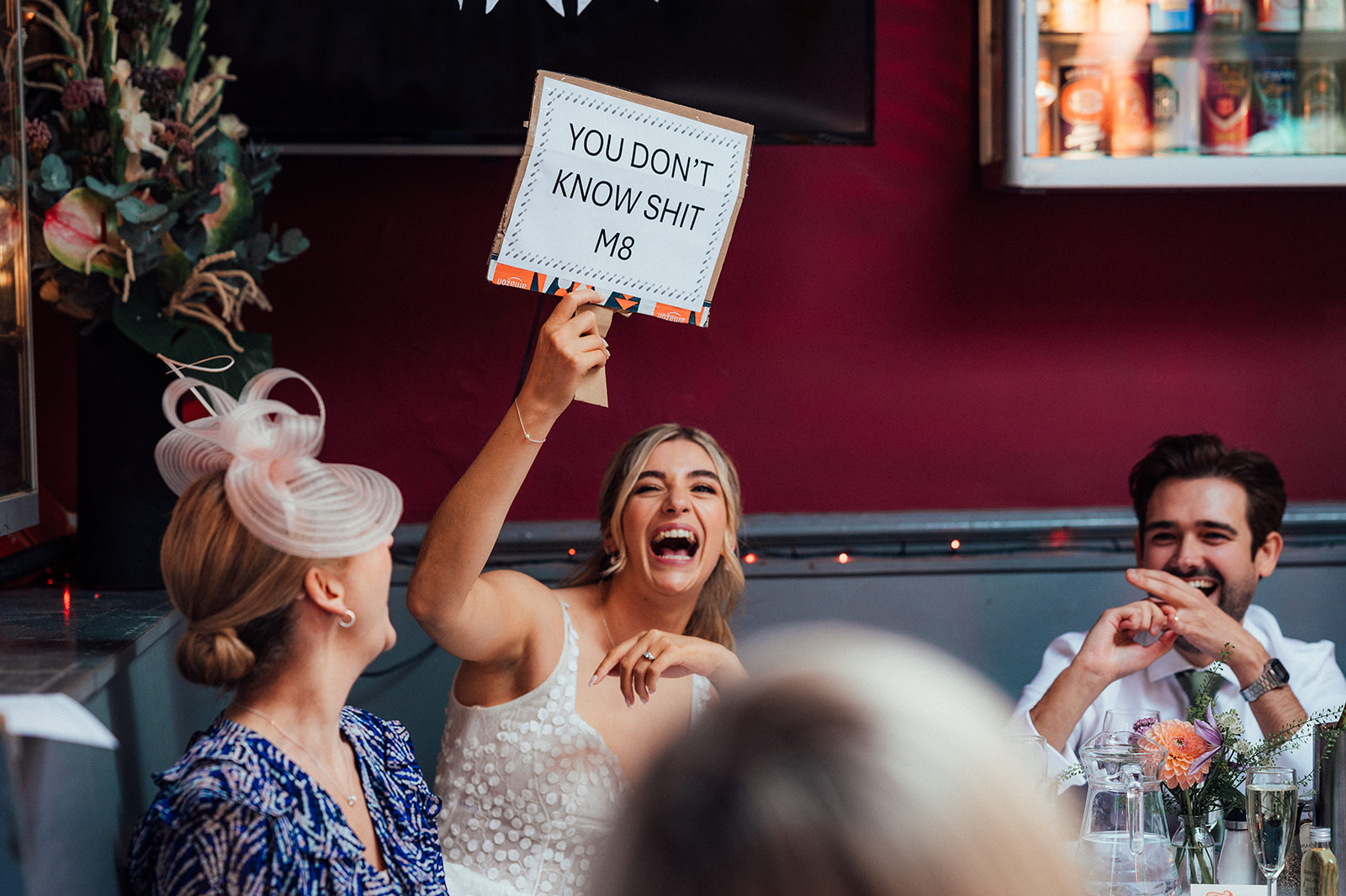 A bride laughing and holding up a sign that says "you don't know shit M8"